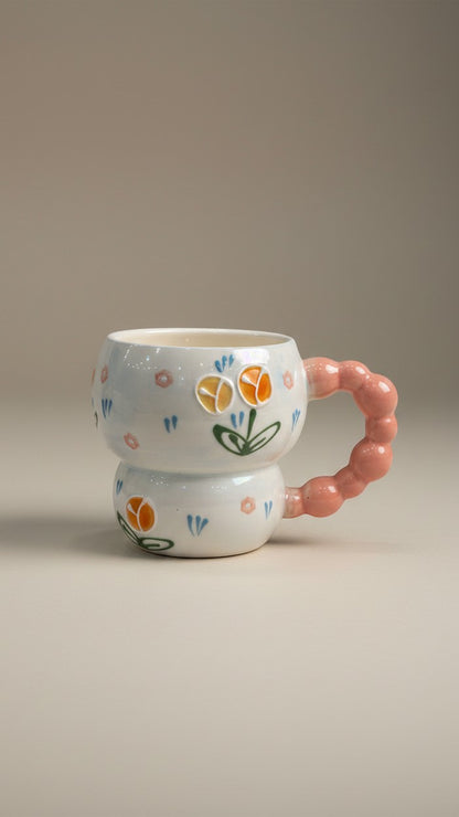 Asoula white ceramic coffee mug with a pink bubble handle and a charming floral design featuring orange and yellow tulips.