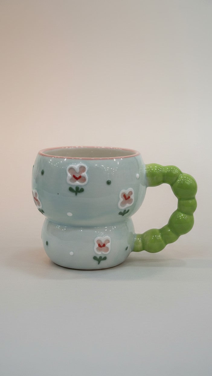 Asoula light blue ceramic mug with a unique green bubble handle and a delicate floral pattern.