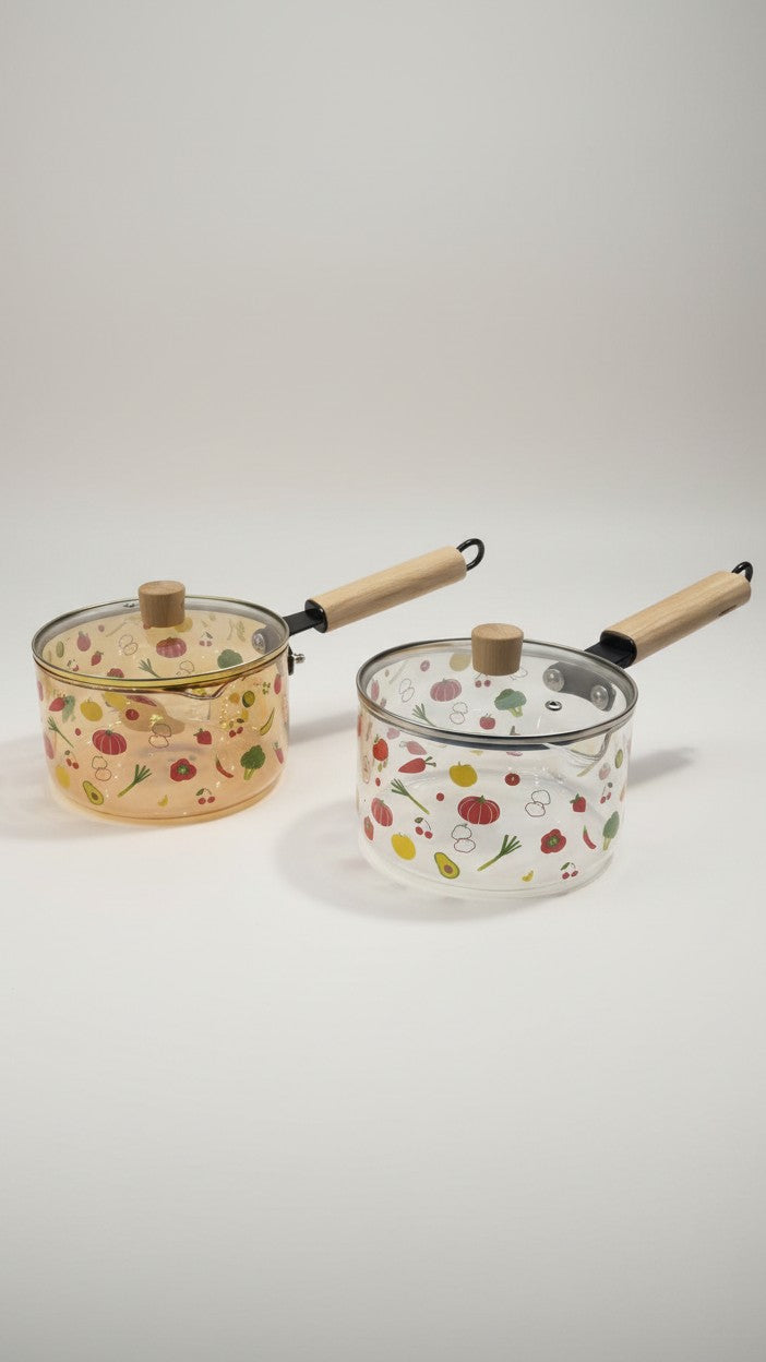 Asoula clear glass saucepan with lid, featuring a playful vegetable print and wooden handle. Oven-safe for versatile cooking.