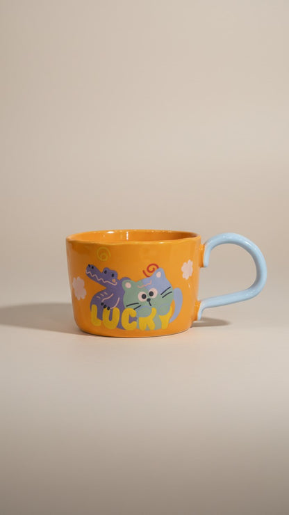 Asoula orange ceramic mug with cute cartoon cat and alligator design, light blue handle.