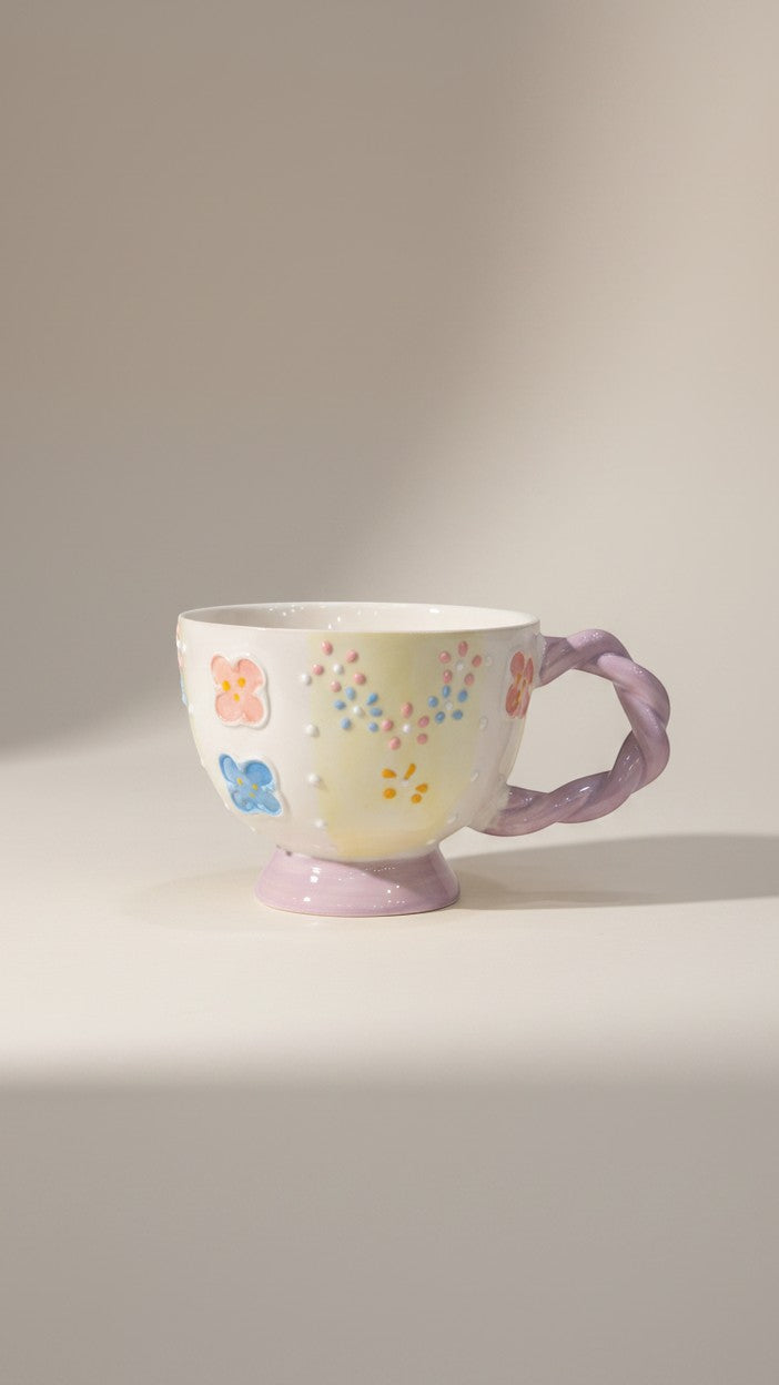 Asoula ceramic mug with pastel floral designs and a twisted lavender handle. Features raised dots and a pedestal base.