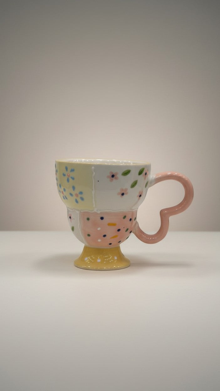 Asoula ceramic mug with patchwork design featuring pastel floral and polka dot patterns, and a pink heart-shaped handle.
